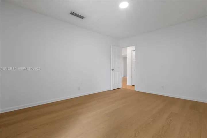 Neutral interior space featuring wood-finish flooring, white walls, and a multi-panel door