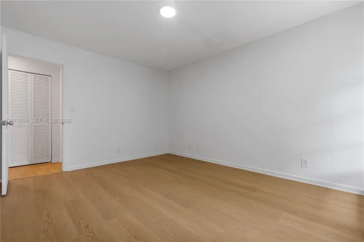 Wood-finish flooring, neutral walls, recessed ceiling lighting, and a closet with white louvered doors