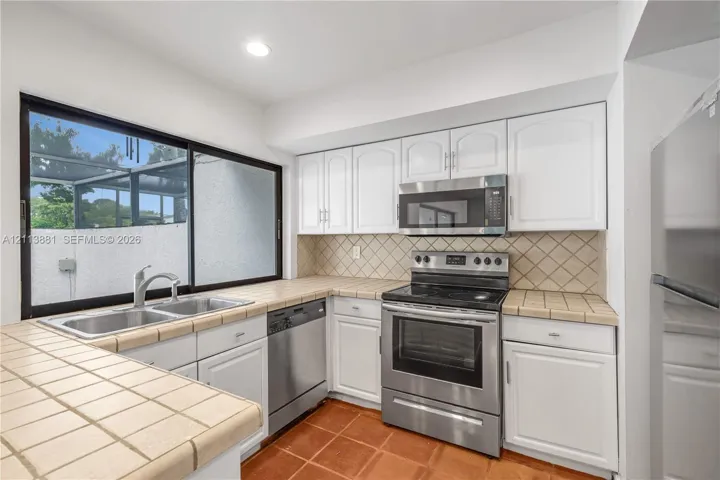 Kitchen featuring white cabinetry, stainless steel appliances, tiled countertops, a double-basin sink, and ceramic tile flooring