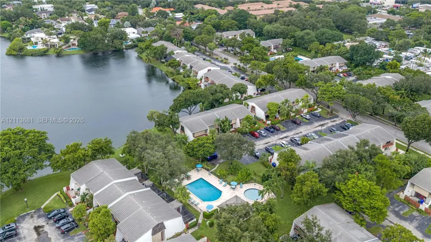 Aerial perspective featuring waterfront placement, community pool, spa, established landscaping, and paved parking