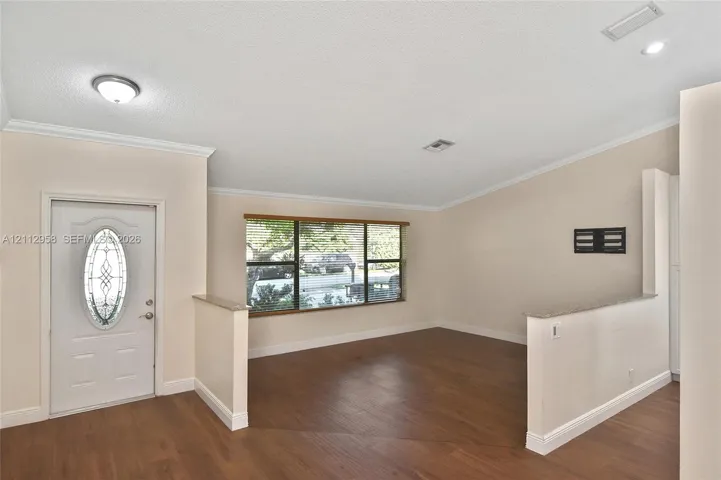 Entryway featuring wood-finish flooring, vaulted ceilings, neutral wall tones, a front door with an oval glass insert, and half-height partition walls with stone-finish caps
