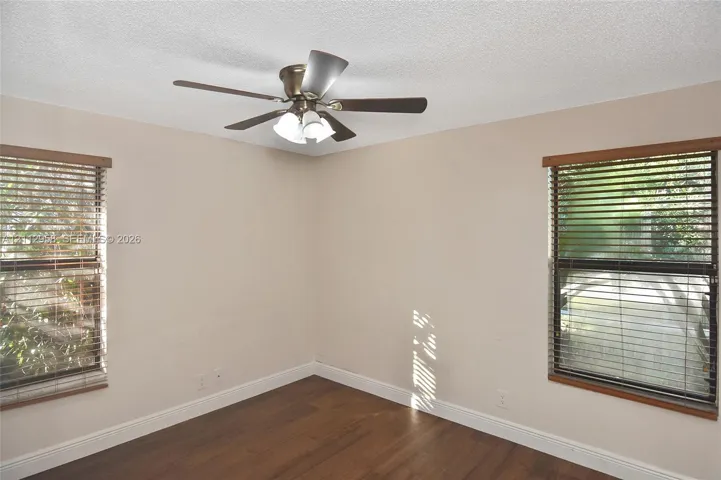 Interior space featuring wood-finish flooring, two dual-pane windows with horizontal blinds, and a multi-blade ceiling fan with an integrated light fixture
