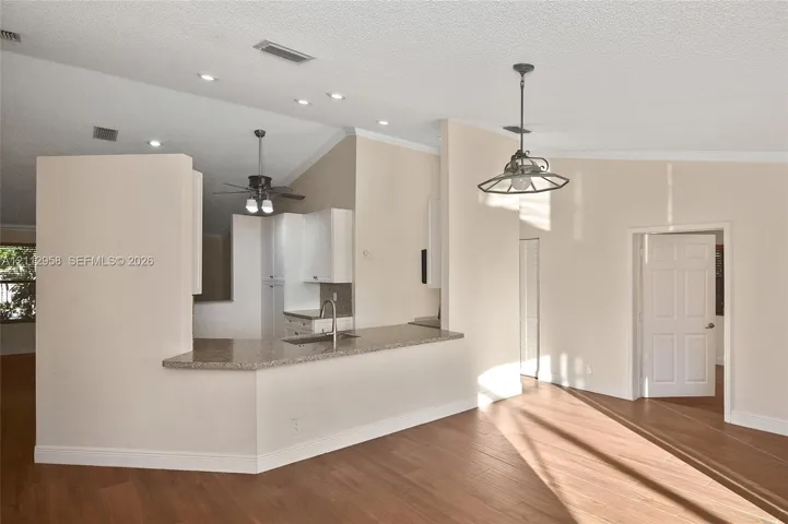 Open-concept kitchen featuring a breakfast bar with stone-finish countertop, stainless steel sink, white cabinetry, wood-finish flooring, and vaulted ceilings with recessed lighting