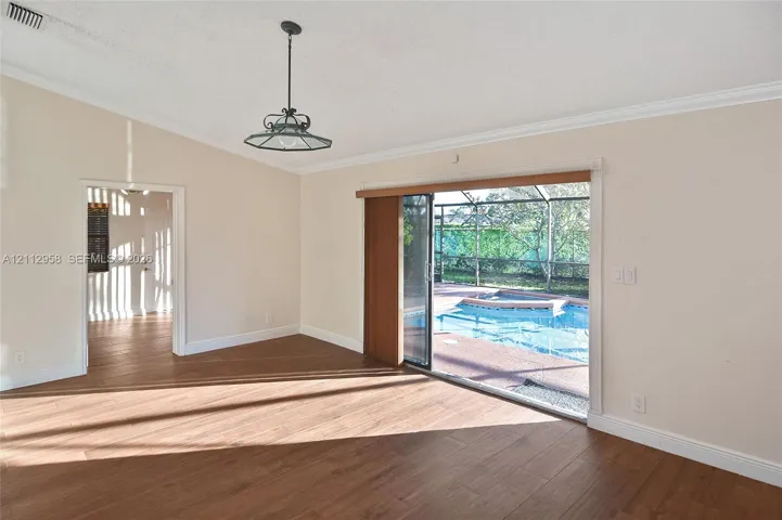 Vaulted ceiling room featuring wood-finish flooring, a decorative metal pendant light, crown molding, and sliding glass doors opening to a screened-in pool area