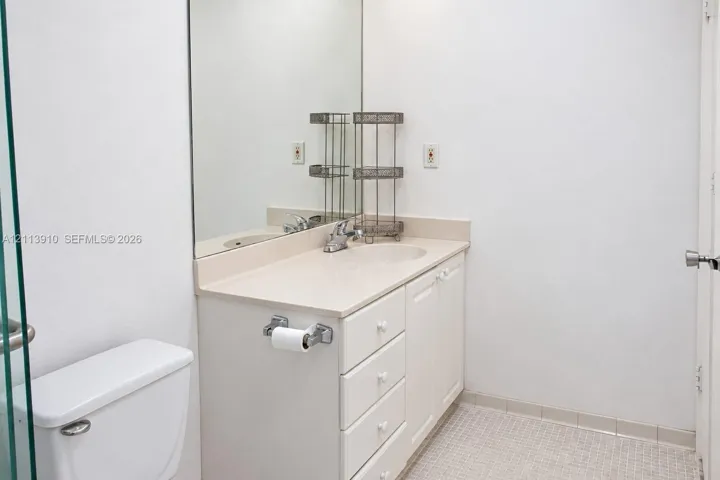 Vanity featuring a solid-surface countertop with an integrated basin, white cabinetry, a large wall-mounted mirror, and tile flooring