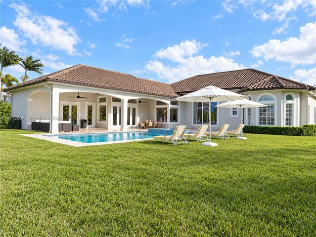 Rear exterior featuring a tile roof, covered patio with recessed lighting, in-ground pool with integrated spa, and expansive lawn