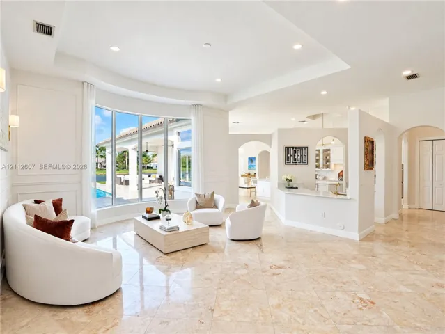 Spacious living area featuring polished stone flooring, a tray ceiling, curved bay windows, and a built-in partition wall with an integrated breakfast bar