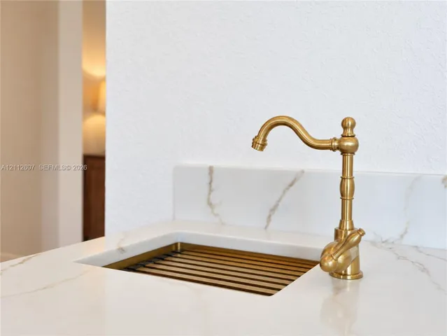Integrated stone-finish countertop with a coordinating backsplash, featuring a custom metal-finish sink basin and a decorative brass-finish gooseneck faucet