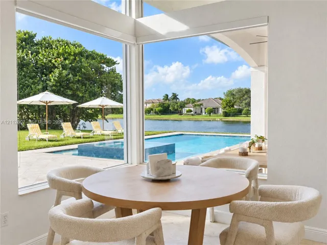 Floor-to-ceiling corner windows showcasing a paved pool deck, a swimming pool with integrated spa, and water frontage