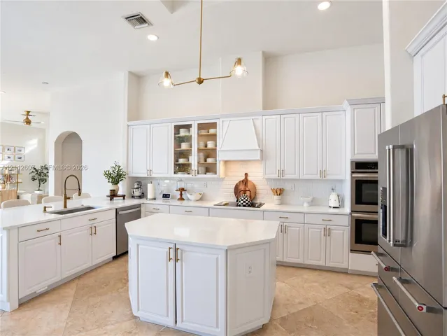 Kitchen featuring white shaker-style cabinetry, central island with stone-finish countertops, stainless steel double wall ovens, brick-pattern backsplash, and stone tile flooring