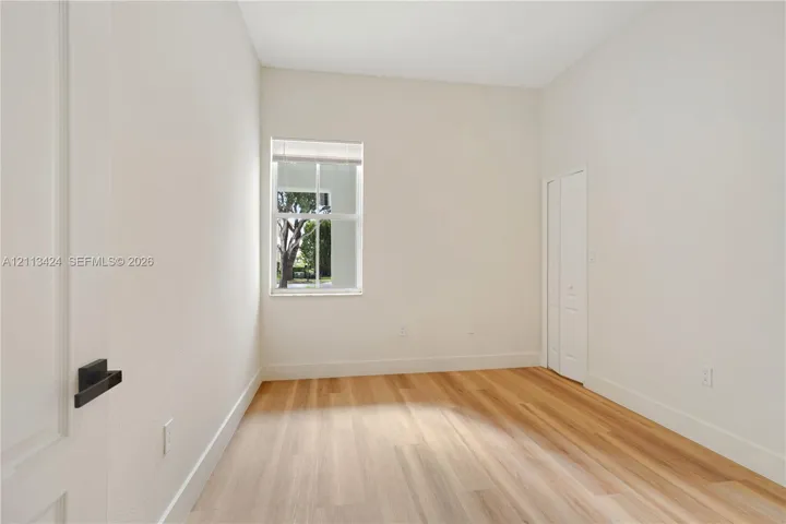 Interior space featuring wood-finish flooring, crisp white walls, a single-pane window with interior muntins, and dual-panel closet doors with matte black hardware