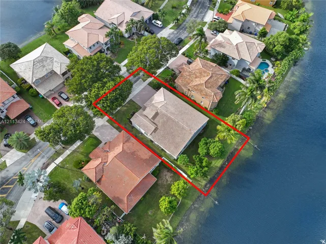Aerial perspective featuring a waterfront lot, multi-hipped tile roof, paved driveway, and mature landscaping