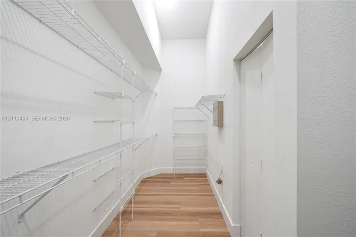 Walk-in closet featuring wood-finish flooring, white walls, vaulted ceiling, and tiered white wire shelving
