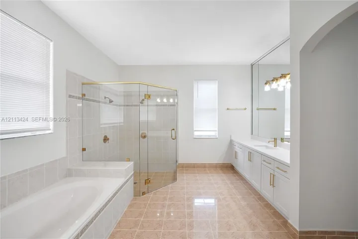 Bathroom featuring a glass-enclosed shower, soaking tub with tile surround, dual-sink vanity with white cabinetry, and large-format wall mirror