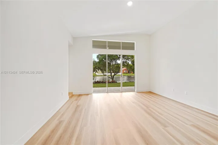 Interior space featuring vaulted ceilings, light-toned wood-finish flooring, and expansive sliding glass doors topped with rectangular transom windows