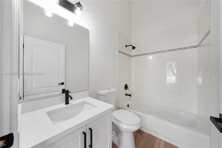 Bathroom featuring a white vanity with a composite countertop, matte black fixtures, a wall-mounted light fixture, and a tub-shower combination with decorative tile inlay