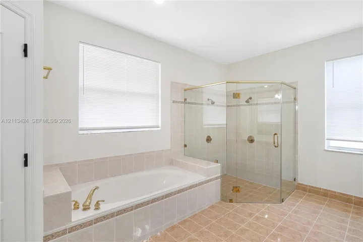 Soaking tub with tiled surround, glass-enclosed shower with gold-tone hardware, and ceramic tile flooring