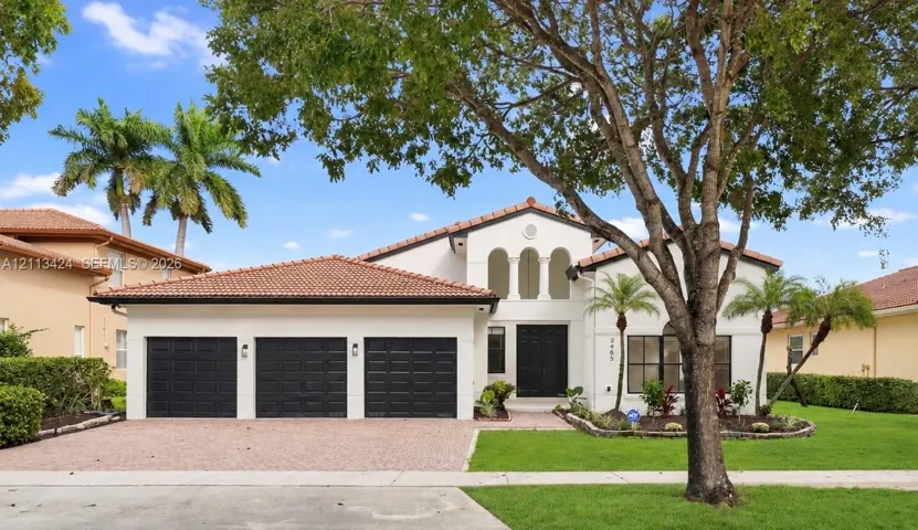 Stucco exterior featuring a clay tile roof, three-car garage, arched architectural detailing, and landscaped grounds