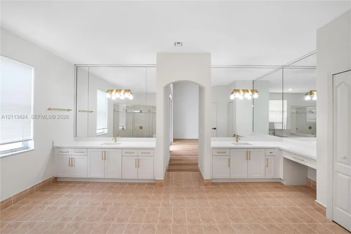 Dual-vanity cabinetry with white countertops, integrated sinks, brass-finish hardware, full-width vanity mirrors, and ceramic tile flooring