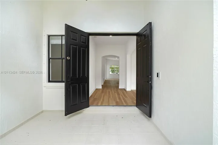 Double front entry doors with black finish, white textured wall exterior, single-pane side window, and interior wood-finish flooring