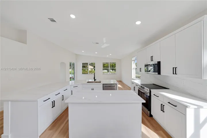 Kitchen featuring white shaker-style cabinetry, quartz countertops with a waterfall-edge center island, integrated stainless steel appliances, and wood-finish flooring