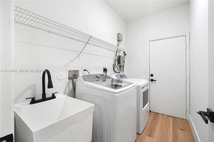 Laundry room featuring wood-finish flooring, a utility sink with a matte black faucet, and an integrated wire wall shelf
