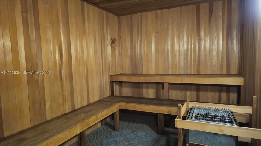 Sauna featuring tongue-and-groove wood paneling, multi-tiered built-in wood benches, and a dedicated heating unit with stone enclosure
