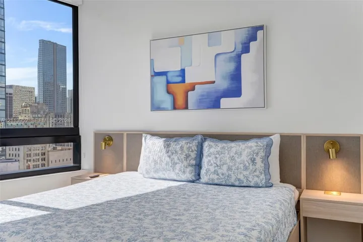 Floor-to-ceiling window, custom wood-paneled headboard with integrated nightstands, and wall-mounted metallic sconces
