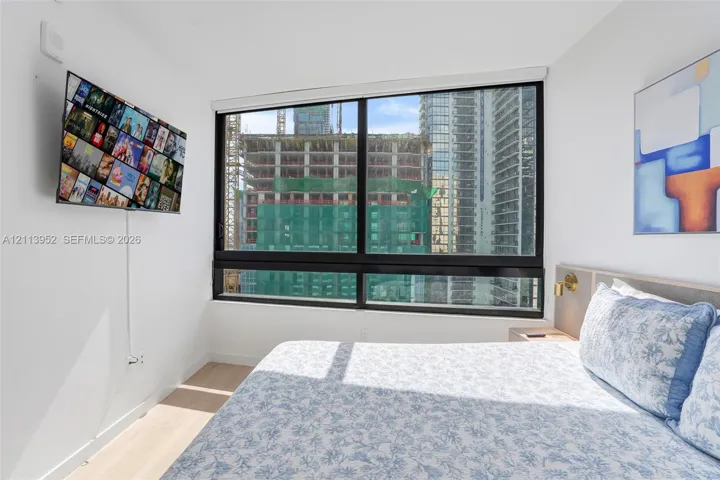 Large-format window with black framing, wood-finish flooring, and built-in headboard featuring integrated brass lighting