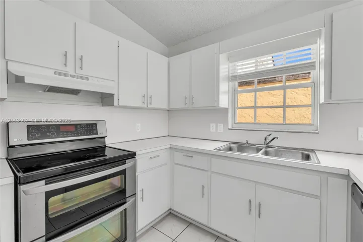 Kitchen featuring white cabinetry, solid-surface countertops, stainless steel double-oven range, integrated range hood, and double-basin stainless steel sink
