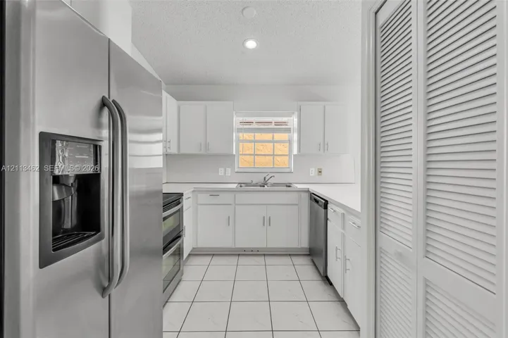 Kitchen featuring stainless steel appliances, white cabinetry, solid-surface countertops, tile flooring, and louvered closet doors
