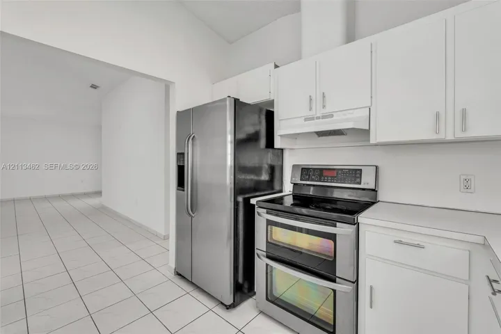 Kitchen featuring white cabinetry, stainless steel double-oven range, stainless steel refrigerator, and tile flooring