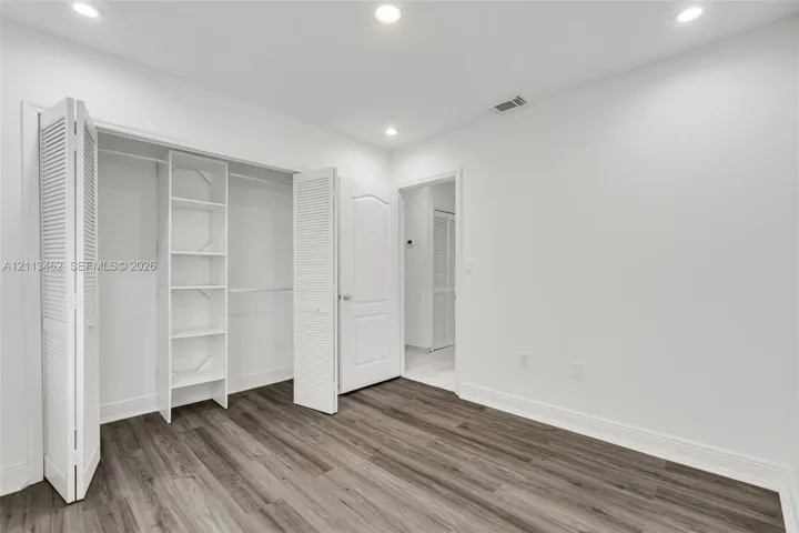 Wood-finish flooring, recessed lighting, and a reach-in closet with integrated shelving and louvered bifold doors