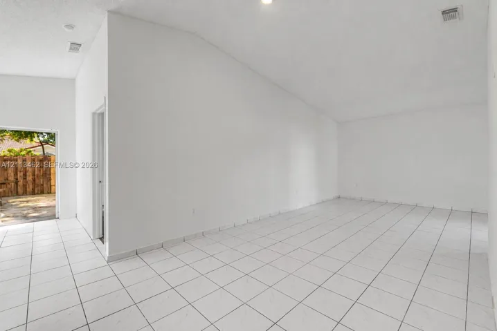 High-ceiling interior space featuring large-format ceramic tile flooring, neutral wall finishes, and an exterior doorway with access to a paved patio area