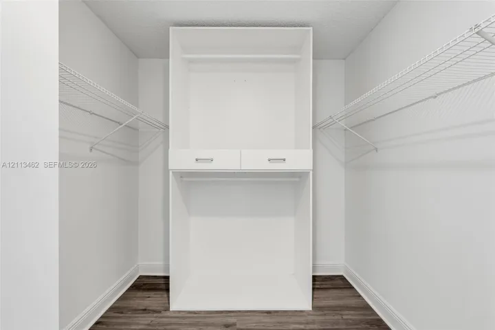 Storage closet featuring white built-in shelving, dual drawers with metal hardware, and dual-level wire racking, complemented by wood-finish flooring