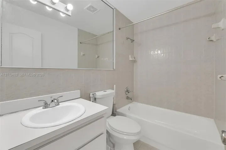 Bathroom featuring a vanity with a white countertop and oval under-mount sink, large wall-mounted mirror, overhead vanity lighting, and a shower-tub combination with ceramic tile surround