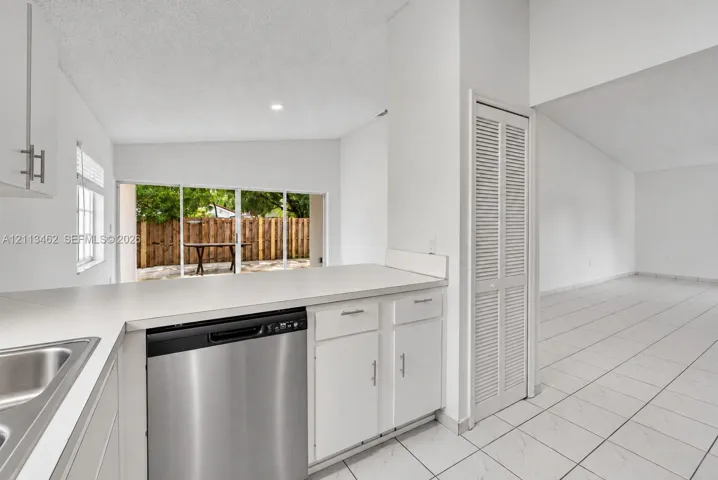 Kitchen featuring white cabinetry, stainless steel dishwasher, solid-surface countertops, floor-to-ceiling louvered-door closet, and neutral tile flooring
