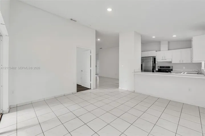 Open-concept interior featuring light-colored tile flooring, recessed lighting, breakfast bar, and stainless steel kitchen appliances