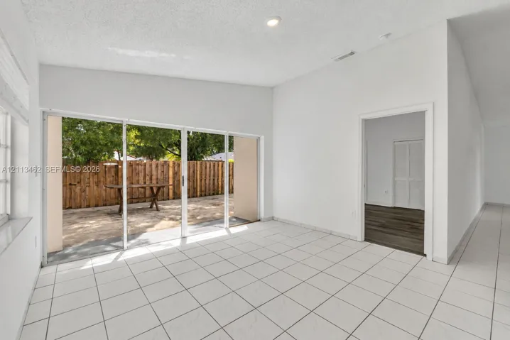 Open-concept room featuring white ceramic tile flooring, vaulted ceilings, recessed lighting, and multi-panel sliding glass doors providing access to a paved patio