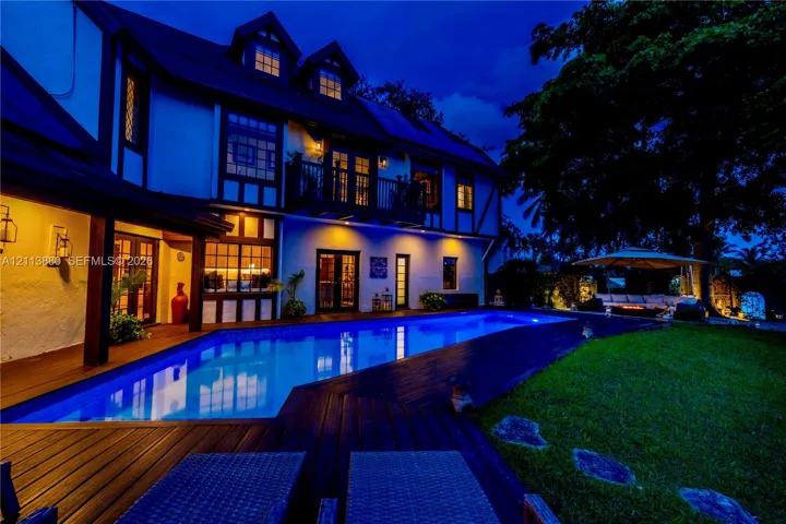 Tudor-style exterior featuring a rectangular inground swimming pool, expansive wood-finish decking, second-story balcony, and steep-pitched roofline with dormer windows