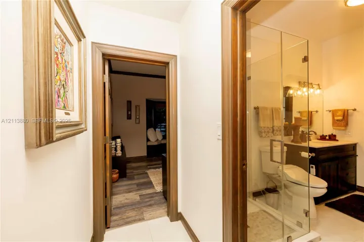 Bathroom featuring a dark wood vanity with a light-toned countertop, a glass-enclosed shower, and a ceramic toilet, framed by wood-trimmed doorways