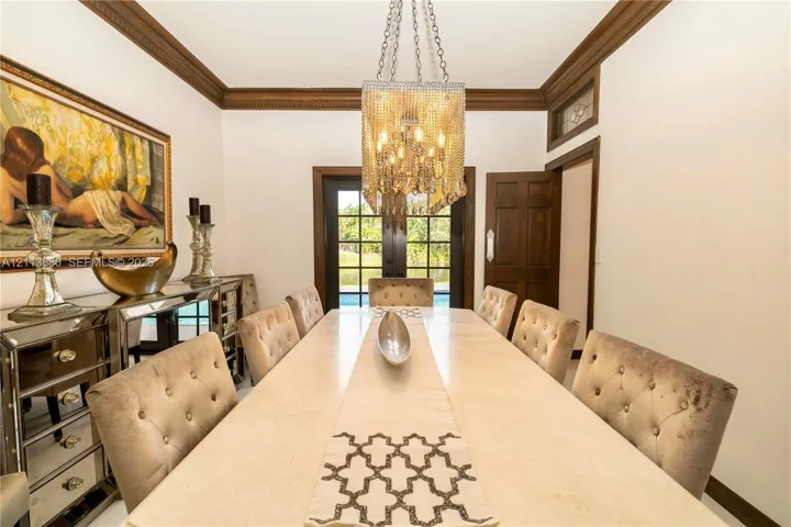 Formal dining area featuring rich wood crown molding, multi-pane glass exterior doors, and a decorative crystal-style chandelier