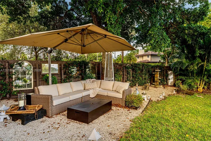 Landscaped backyard featuring a gravel patio area, perimeter wood fencing with integrated wall mirrors, tiered stone fountain, and mature tree canopy