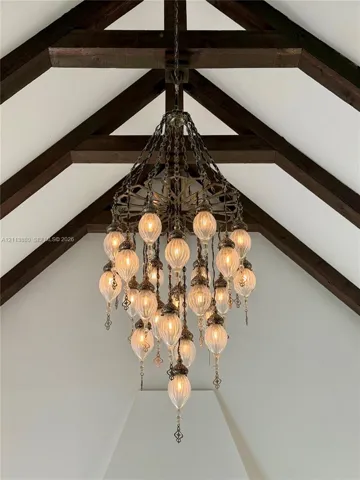Vaulted ceiling featuring exposed timber beams and a multi-tiered metal chandelier with scalloped glass fixtures