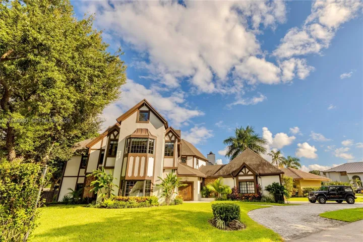 Tudor-style exterior featuring multi-gabled rooflines, decorative timber framing, a prominent multi-level bay window, and a gravel driveway