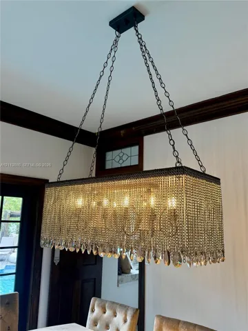 Rectangular chandelier featuring tiered crystal fringe, metal chain suspension, dark wood crown molding, and a transom window with leaded glass detail