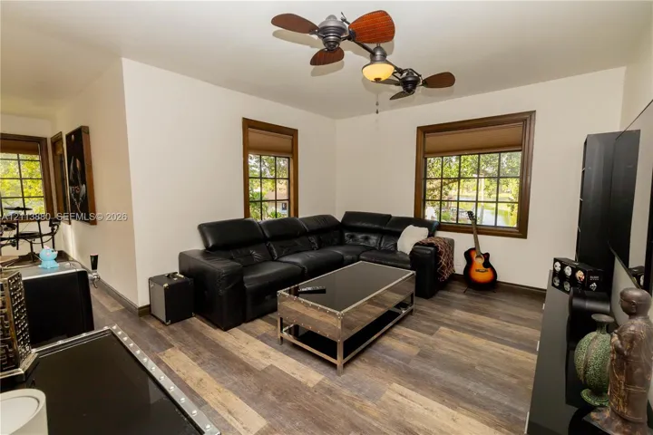Wood-finish flooring, multi-pane windows with dark wood trim, and a dual-motor ceiling fan with integrated lighting