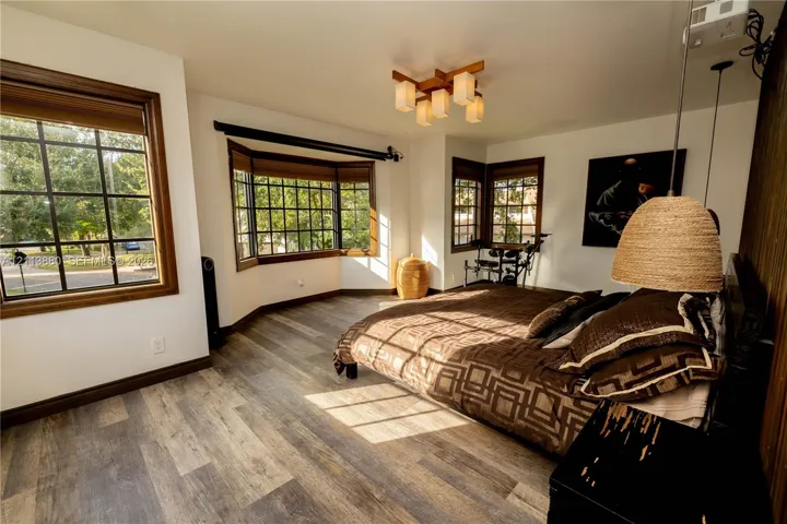 Wood-finish flooring, multi-pane windows with wood-tone casing, bay window, geometric-style multi-light ceiling fixture, and wood-paneled accent wall
