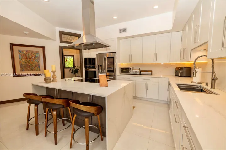 Kitchen featuring white flat-panel cabinetry, a central island with quartz surfacing, stainless steel appliances, a stainless steel range hood, and tile flooring