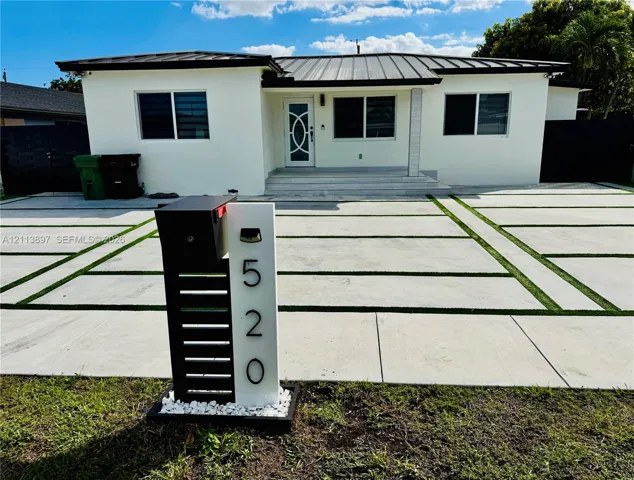 Single-story exterior featuring a metal roof, smooth stucco facade, custom decorative front door, and a geometric concrete driveway with integrated turf accents